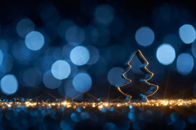 Still life photography of an abstract Christmas background. Christmas tree cookie cutter on golden shiny glitter, lens flares, and defocused blue lights. Native image size: 7952x5304