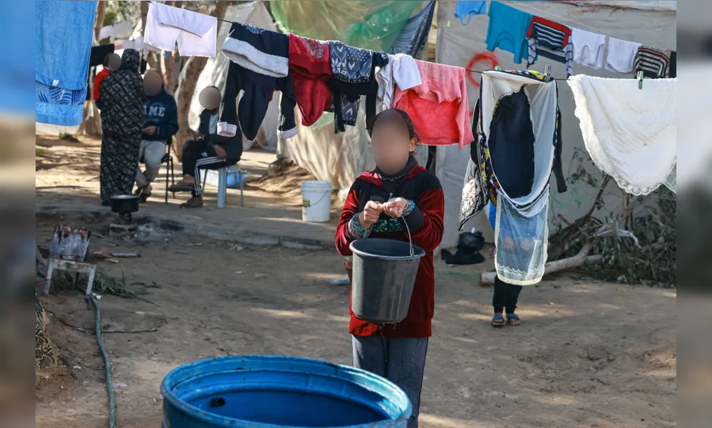Criança carrega balde de água em campo de refugiados em Rafah, na Faixa de Gaza