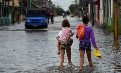 Children walk through flooded waters after the passage of hurricane Rafael in Batabano, Artemisa province, Cuba on November 7, 2024. Power was restored to parts of Cuba on Thursday a day after Hurricane Rafael swept over the island, leaving its 10 million inhabitants without electricity for the second time in a month. (Photo by YAMIL LAGE / AFP)