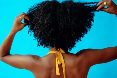 back shot of a young adult woman with hands on her curly black hair