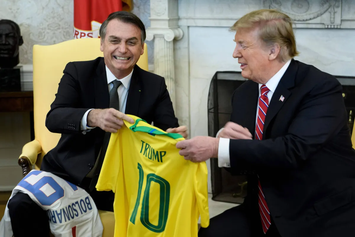 Brazil's President Jair Bolsonaro (L) and US President Donald Trump present each other with their national soccer team jerseys before a meeting in the Oval Office of the White House March 19, 2019 in Washington, DC. (Photo by Brendan Smialowski / AFP)
