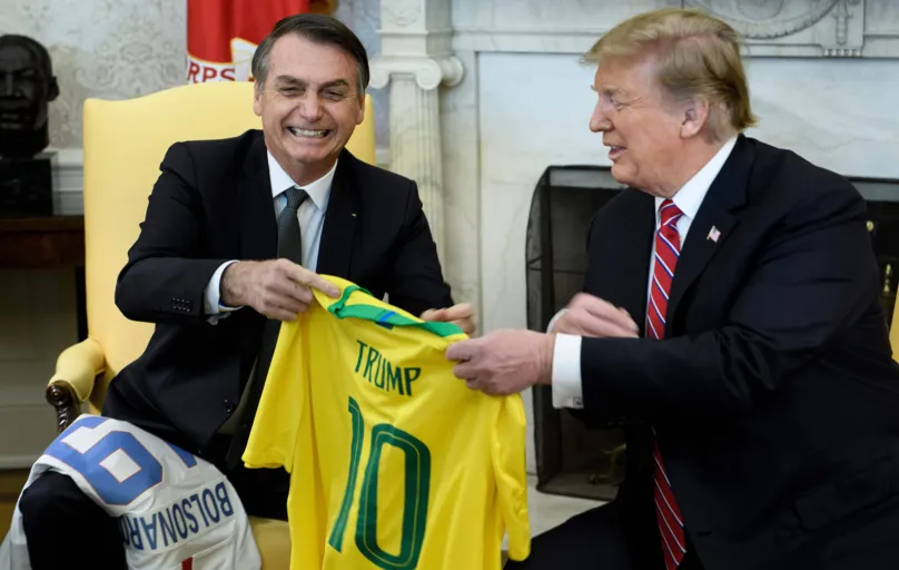 Brazil's President Jair Bolsonaro (L) and US President Donald Trump present each other with their national soccer team jerseys before a meeting in the Oval Office of the White House March 19, 2019 in Washington, DC. (Photo by Brendan Smialowski / AFP)