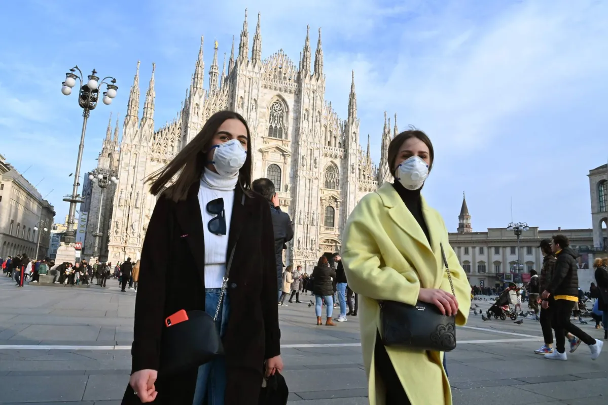 Mulheres usam máscaras respiratórias enquanto caminham pela  Piazza del Duomo , na área central de Milão
