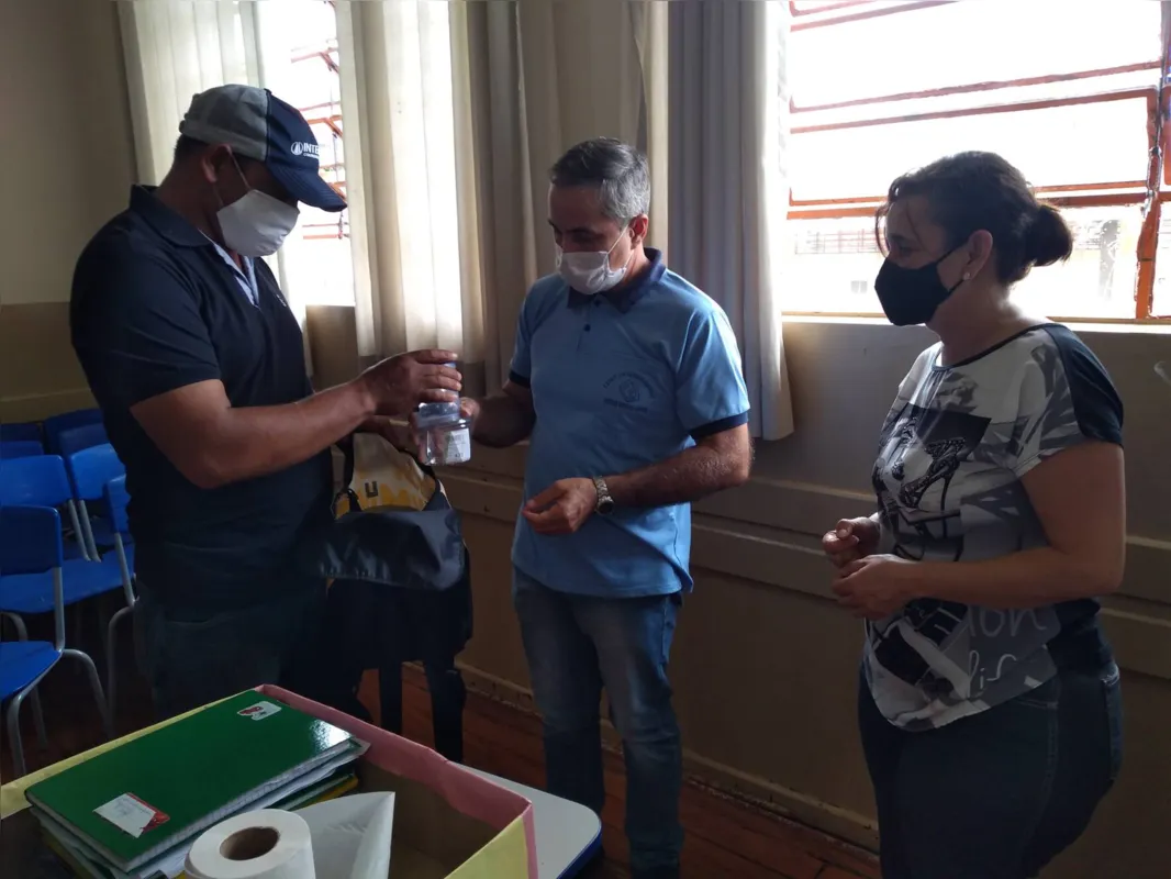 O diretor Marco Aurélio de Carvalho e a coordenadora da Escola Municipal Professora Corina Mantovan Okano entregando o material  escolar  a um pai de aluno