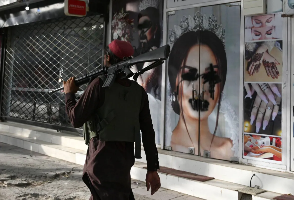 Combatente do Taleban passa por um salão de beleza com a imagem de uma mulher desfigurada por tinta spray: costumes no Afeganistão vão sofrer mudanças drásticas sobretudo para as mulheres