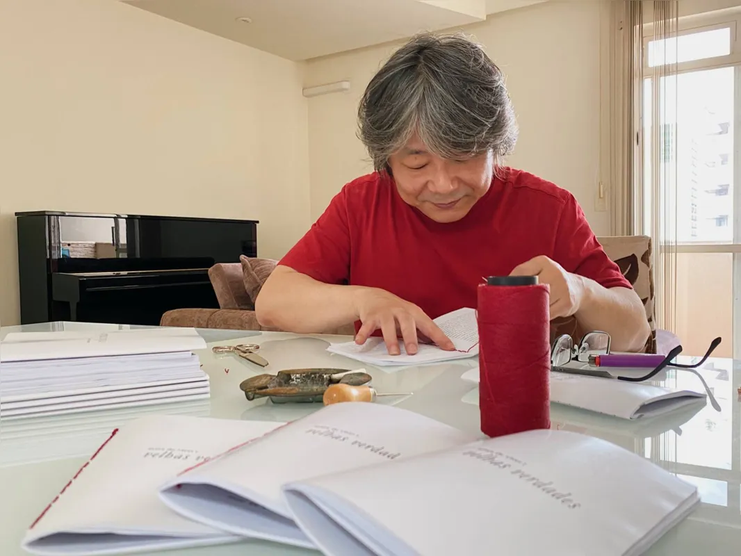 O escritor Tony Hara costurando as páginas de seu novo livro "Artes de viver/Velhas verdades"
