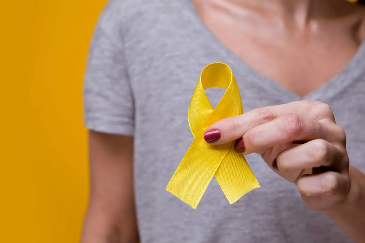 Woman with yellow ribbon on color background. Cancer awareness concept