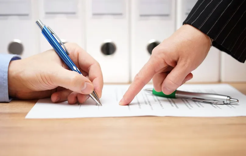 business woman is pointing where to sign on document, with documents in background