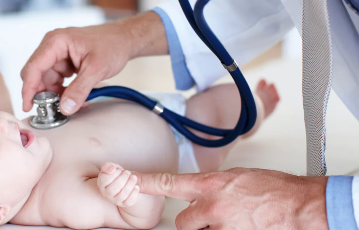 Delighted baby girl smiles at her pediatrician as he examines her chest with a stethoscope