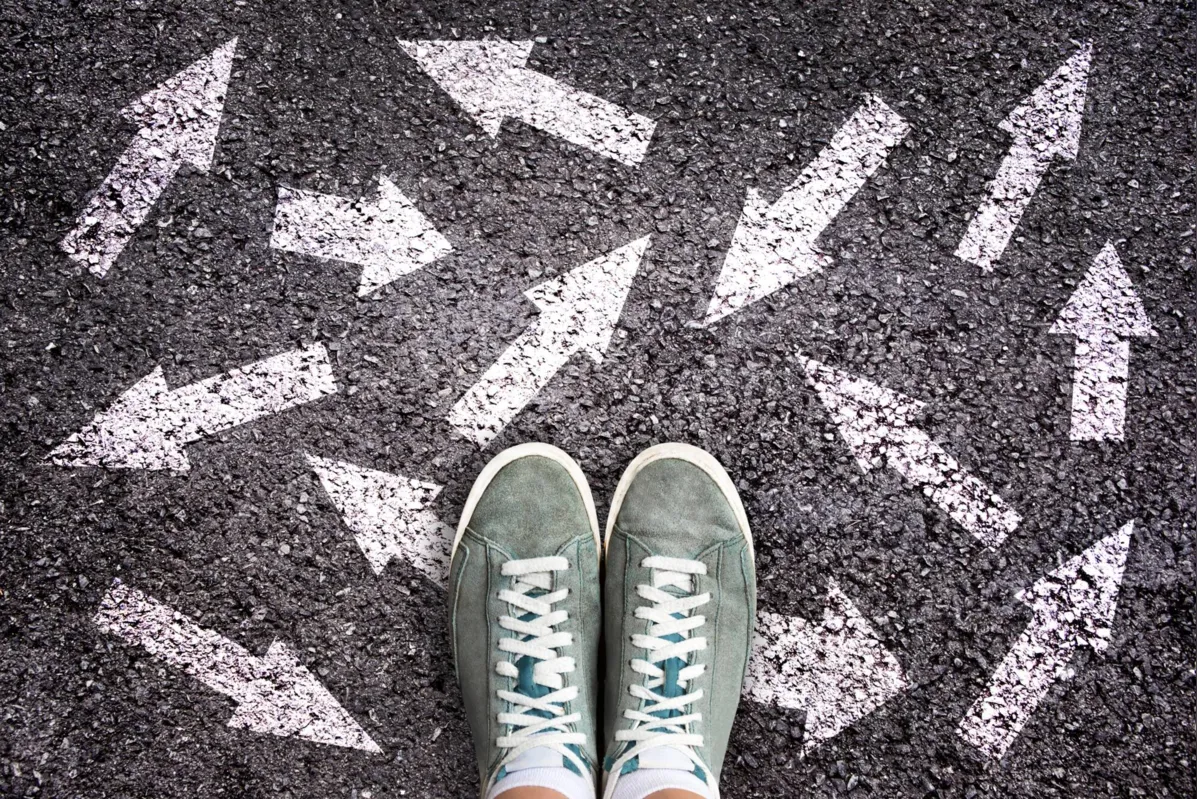 Sneaker shoes and arrows pointing in different directions on asphalt ground, choice concept