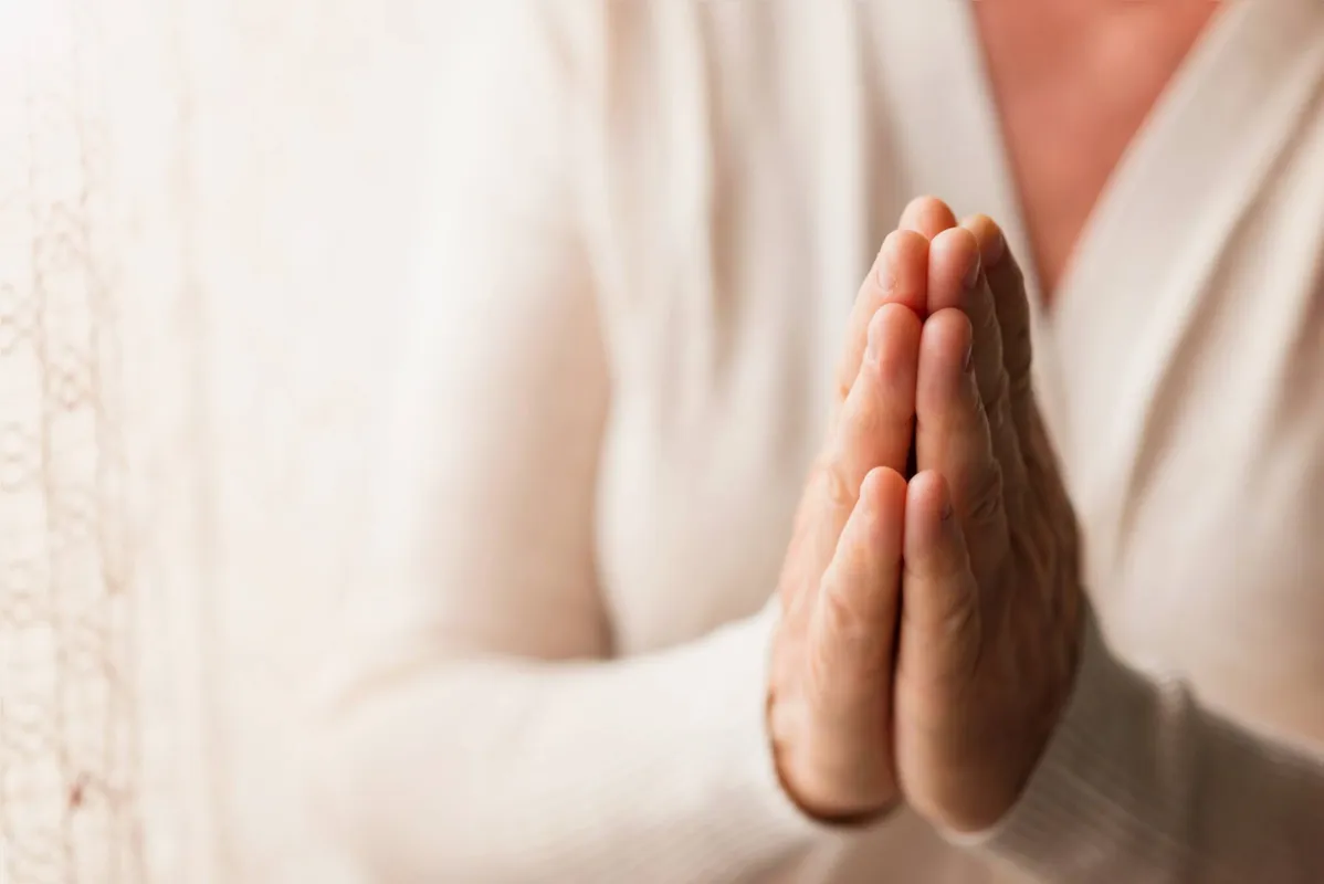Hands of an unrecognizable woman in white cardigan praying