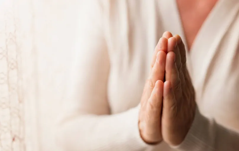 Hands of an unrecognizable woman in white cardigan praying