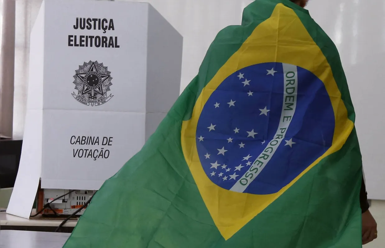 A man wrapped in a Brazilian flag prepares to cast his vote during the legislative and presidential election, in Sao Paulo, Brazil, on October 2, 2022. - Voting began early Sunday in South America's biggest economy, plagued by gaping inequalities and violence, where voters ar expected to choose between far-right incumbent Jair Bolsonaro and leftist front-runner Luiz Inacio Lula da Silva, any of which must garner 50 percent of valid votes, plus one, to win in the first round. (Photo by Miguel Schincariol / AFP)