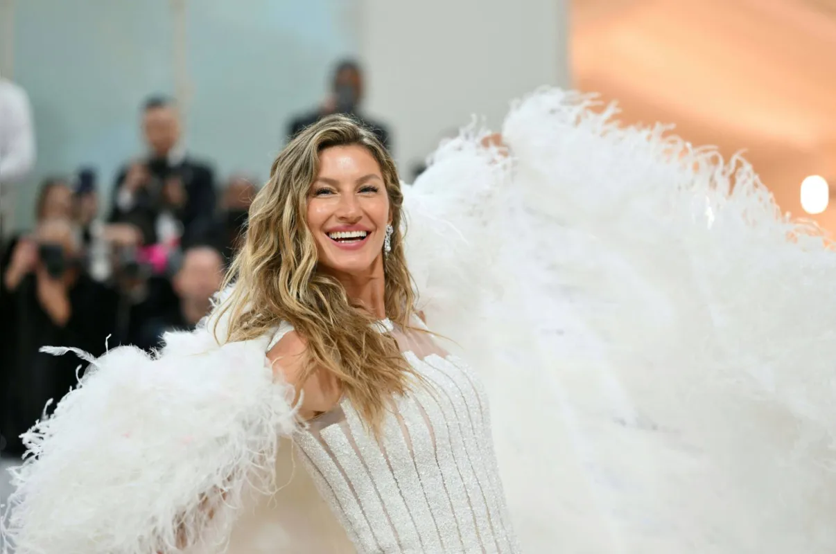 Gisele Bündchen
apareceu no tapete vermelho do evento de moda usando um longo vestido branco, com cintura justa e uma capa felpuda com cauda longa nas costas