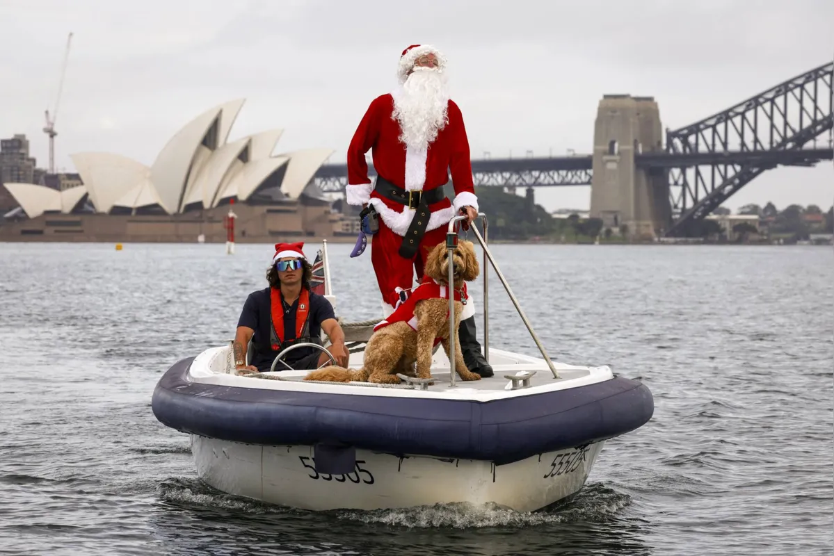 Um homem vestido de Papai Noel anda de barco com seu cachorro em frente à Ópera de Sydney, como parte das comemorações do dia de Natal da corrida anual de iates de Sydney, na Austrália