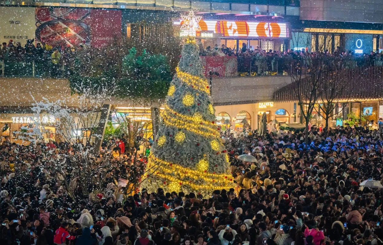 Pessoas reunidas em torno de uma árvore de Natal em uma área comercial com neve artificial no município de Chongqing, no sudoeste da China