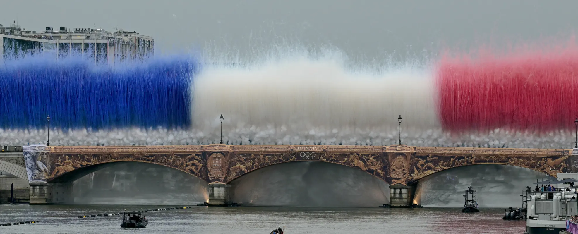 Fogos de artifício com as cores nacionais francesas explodem sobre Pont d'Austerlitz durante a cerimônia de abertura