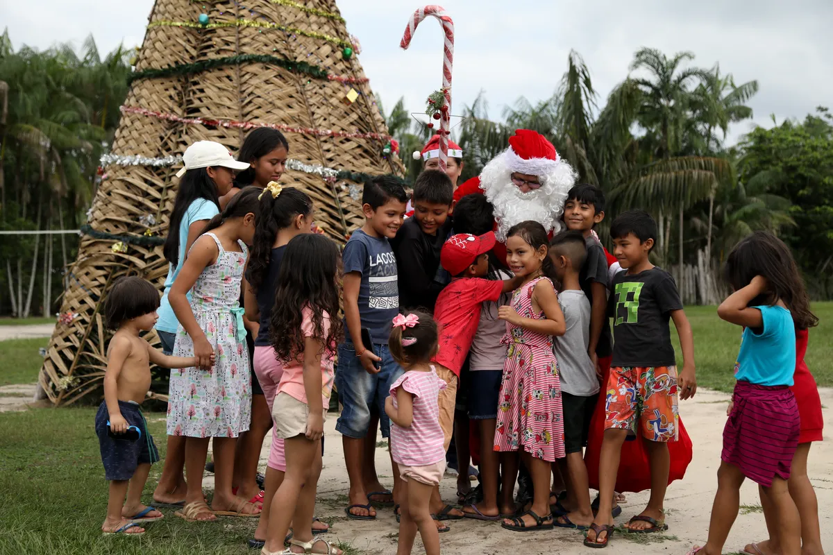 O voluntário Jorge Alberto Barroso, fantasiado de Papai Noel, é recebido por crianças quando chega para entrega de presentes na comunidade ribeirinha de Abelha, em  Manaus (AM). Desde 1998, o grupo  “Amigos Papai Noel vem promovendo o Natal para crianças de comunidades rurais e ribeirinhas da floresta amazônica