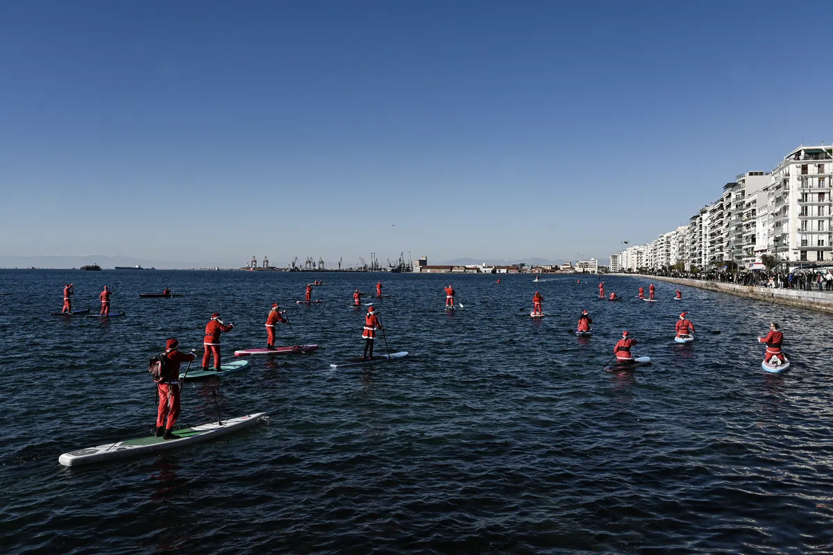 Membros do "ThesSUP" remam ao longo da costa da cidade durante um evento de paddleboarding chamado "The Santa SUP", em Thessaloniki, na Grécia