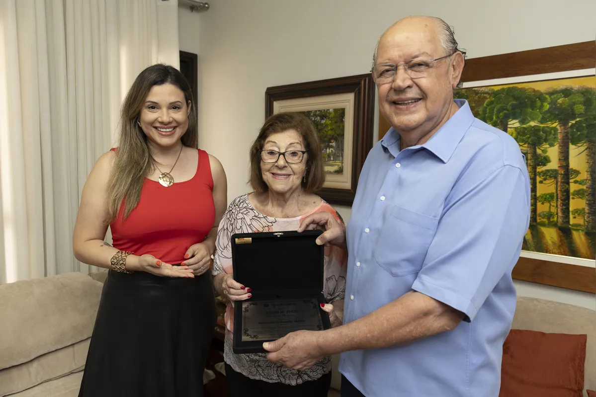 A apresentadora Ana Maziero entrega a placa para o deputado Luiz Carlos Hauly e a irmã dele, Nágila, a primeira criança registrada em Londrina