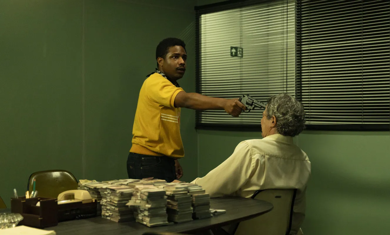 Christian Malheiros como Moreno, o mentor do assalto, pondo a mão no dinheiro na agência bancária