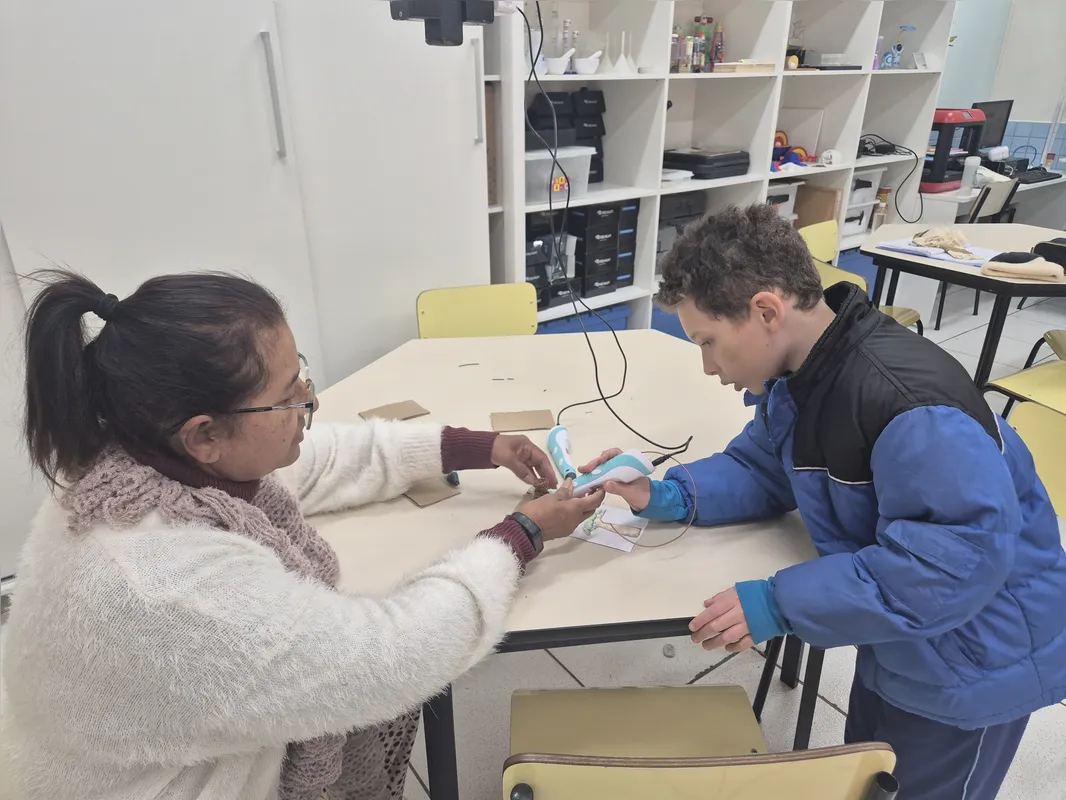 Aluno usando uma caneta 3D com auxílio da professora na sala MakerSpace, dedicada ao uso de tecnologias