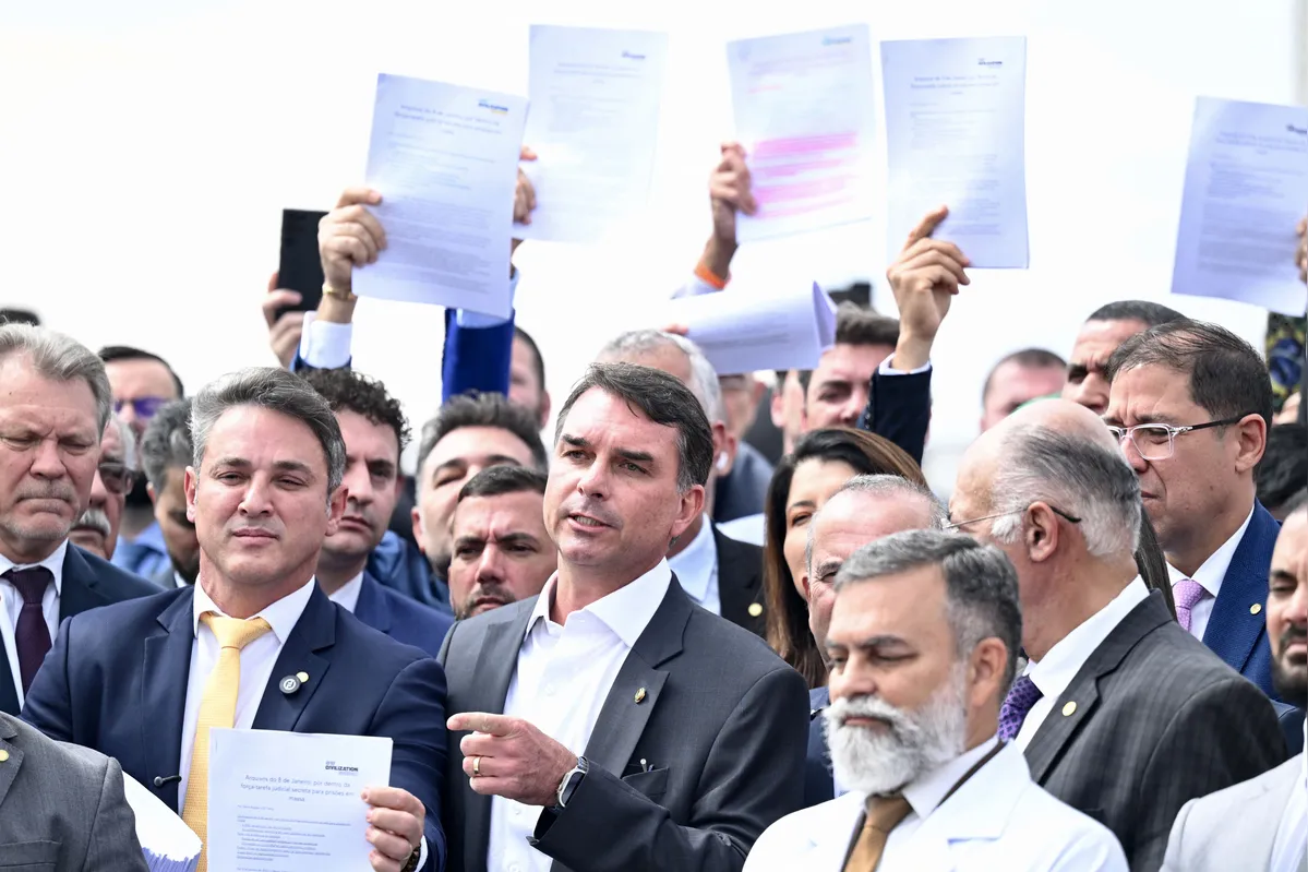 Brazilian Senator Flavio Bolsonaro (C) speaks during a press conference held by opposition lawmakers in support of former Brazilian President Jair Bolsonaro in front of the National Congress in Brasilia on August 5, 2024. A Brazilian judge on August 4 placed former president Jair Bolsonaro under house arrest for breaking a social media ban, escalating a dramatic standoff between the court and the politician, who is accused of plotting a coup. (Photo by EVARISTO SA / AFP)
