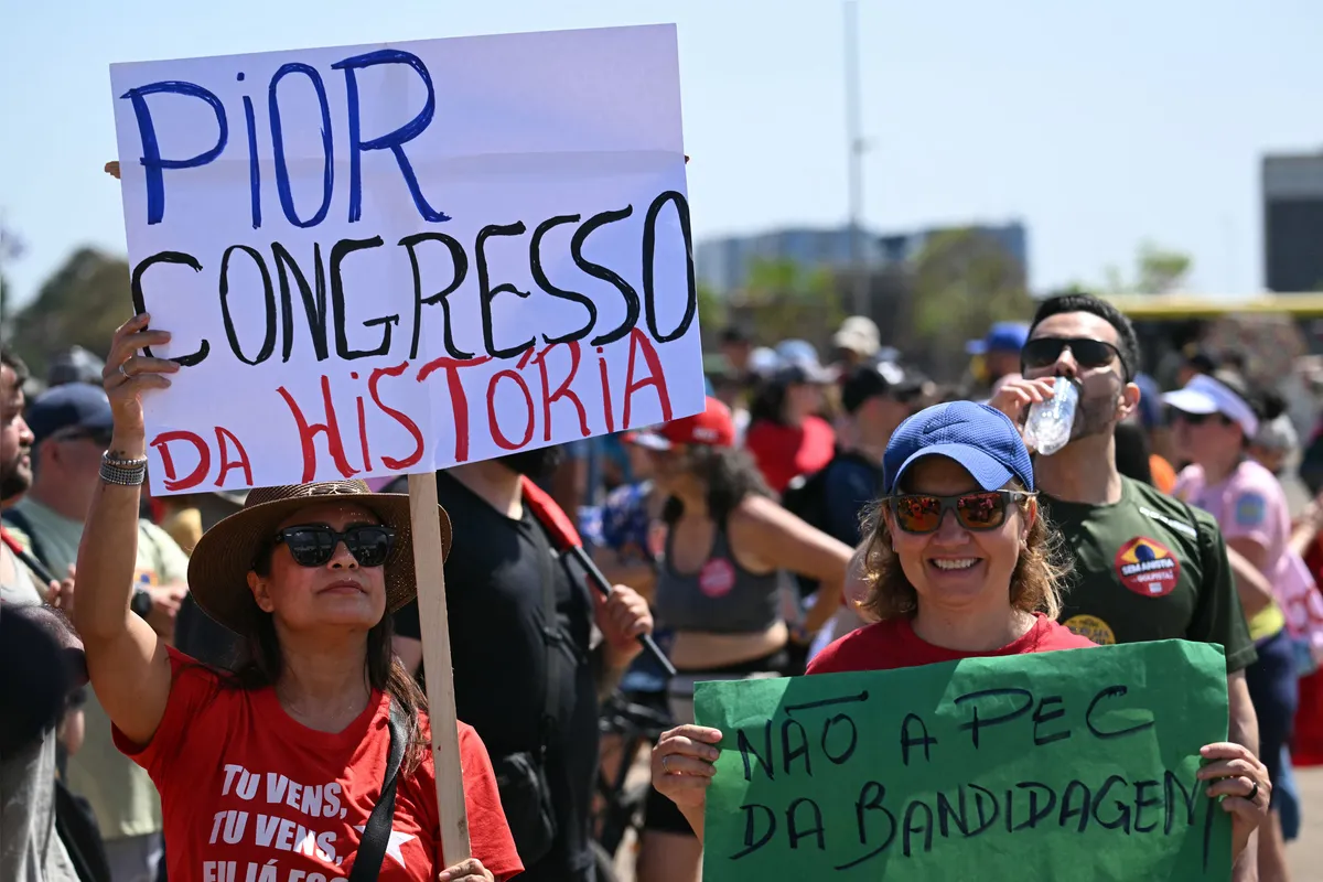 Women hold signs reading "Worst Congress in history" and "No to the bandit's PEC (Proposals to amend the Constitution) during a protest against a constitutional amendment known as the Shielding Project, which requires Congress to authorize any criminal charges against deputies and senators through a secret vote, in Brasilia, on September 21, 2025. Earlier this week, Brazil's Chamber of Deputies, with a conservative majority, approved a parliamentary initiative that extends immunity for legislators and an amnesty project that could benefit far-right former president Jair Bolsonaro, sentenced to 27 years in prison for coup-plotting. (Photo by EVARISTO SA / AFP)