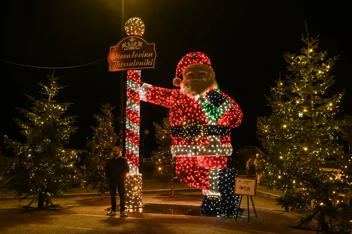Um homem posa para fotos ao lado de um Papai Noel gigante iluminado em Tessalônica