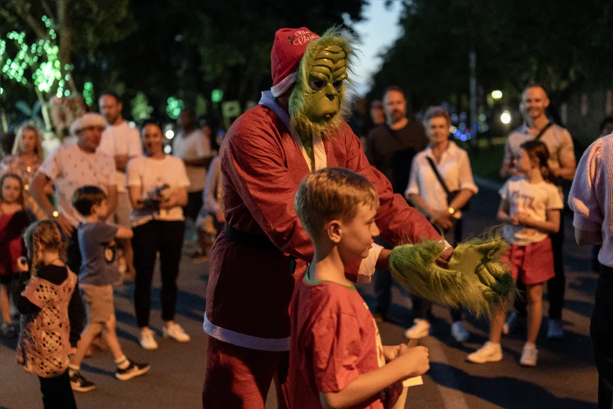 Um homem vestido de Grinch interage com crianças na rua, no bairro de Bryanston, perto de Joanesburgo, na África do Sul