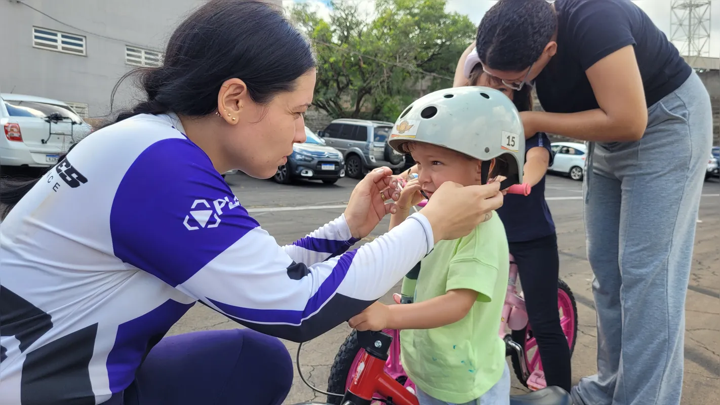 A atleta Eloisa Kalocsay ajuda aluno a vestir capacete para o início da aula
