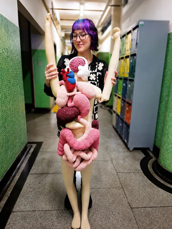 Helena Medeiros, autora do livro, com um trabalho em crochê feito por ela que reproduz os órgãos humanos